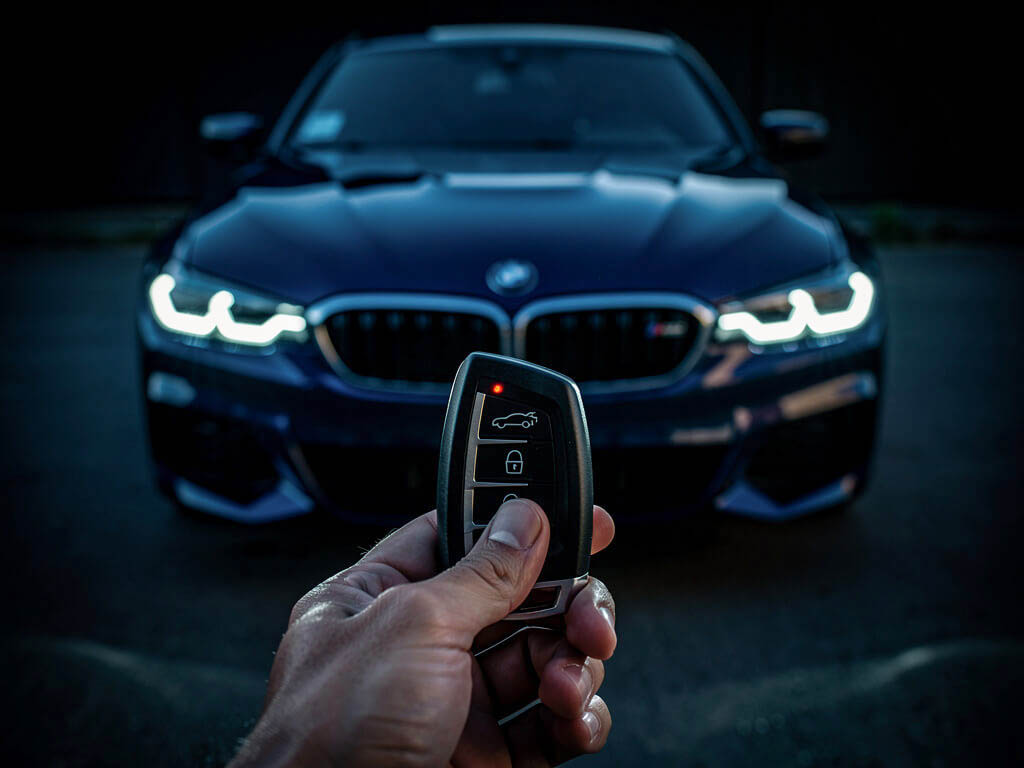 Serrurier automobile d'urgence 24H/24 à Paris et Île-de-France pour vos clés de voiture: main tenant une télécommande BMW devant une berline bleue, phares allumés